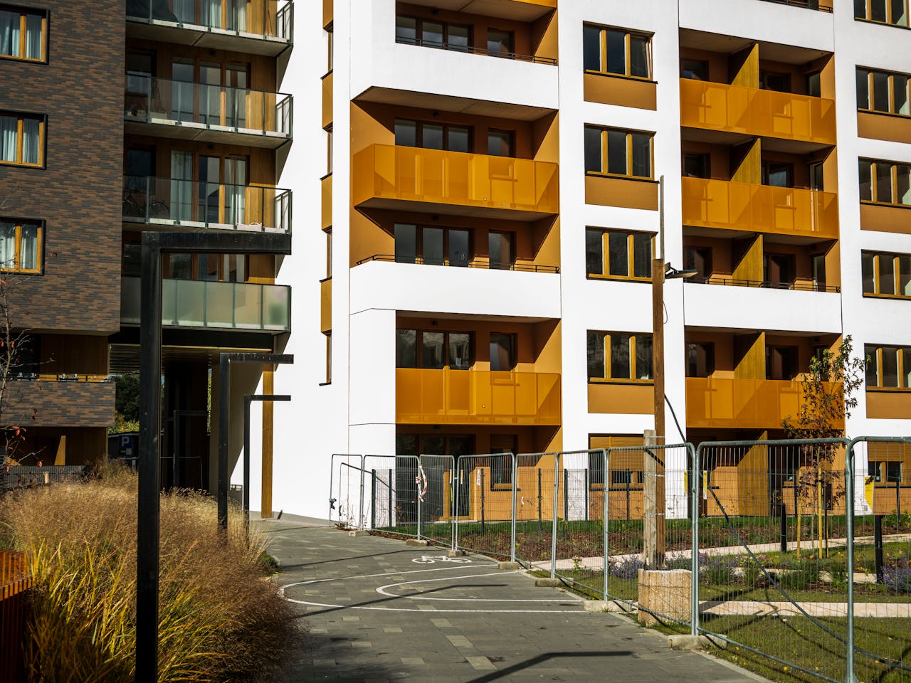 gallery-6 Stylish modern apartment building exterior with golden balconies and a sunny pathway.